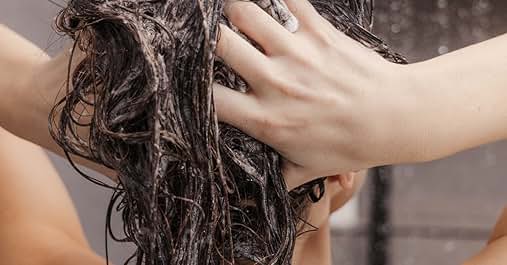 Demostración de la técnica de lavado del cabello con las manos masajeando el champú en el cabello oscuro y húmedo. La espuma y la espuma son visibles en todo