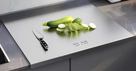 Large stainless steel cutting board with sliced green vegetables and knife on grey counter surface.