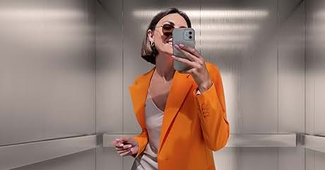Persona que lleva un blazer naranja vibrante sobre una blusa de color claro y se hace una selfie con un teléfono inteligente en un ascensor. El individuo sonríe y lleva gafas