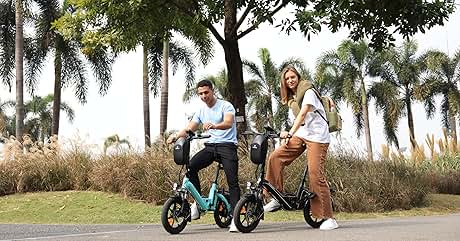 Dos personas montando bicicletas eléctricas plegables de color verde azulado en un sendero. Palmeras y césped en el fondo. El hombre viste camisa blanca y pantalones oscuros, la mujer viste pantalones cortos blancos y lleva una mochila.