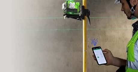 Nivel láser verde que proyecta una línea horizontal en la pared. Persona que sostiene el teléfono inteligente de la mano, posiblemente usándolo junto con el nivel láser
