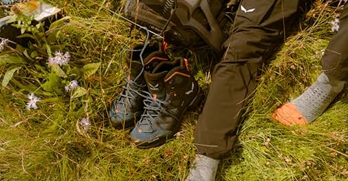 Nahaufnahme von Wanderschuhen auf grasbewachsenem Boden mit kleinen weißen Blumen, was auf ein Trekking im Freien oder einen Spaziergang in der Natur hindeutet