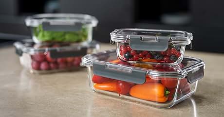 Glass food storage containers with airtight lids. Containers hold various fresh produce: orange bell peppers, red berries, and leafy greens. Stackable design on wooden surface.