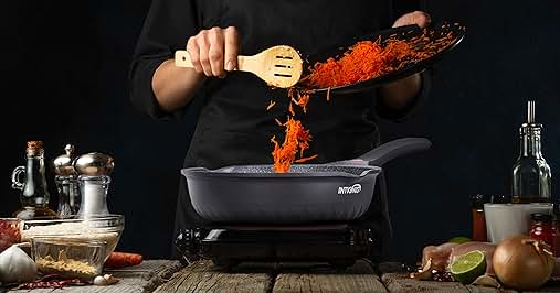 Cast iron skillet on portable stove with spices being dramatically added. Wooden cooking utensils and ingredients surround the cooking scene against a dark background.