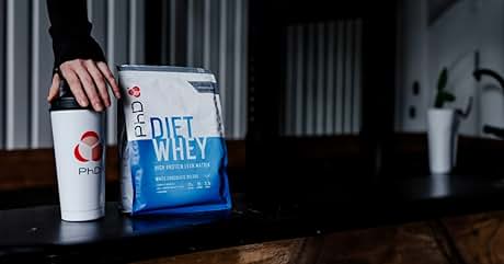 Diet whey protein package in blue and white design, displayed next to a white shaker bottle on wooden surface.