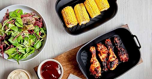 Overhead view of meal prep containers with salad, corn on the cob, and chicken wings. Dipping sauces in small bowls.