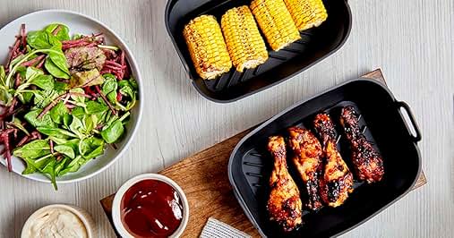 Overhead view of meal prep containers with salad, corn on the cob, and chicken wings. Dipping sauces in small bowls.
