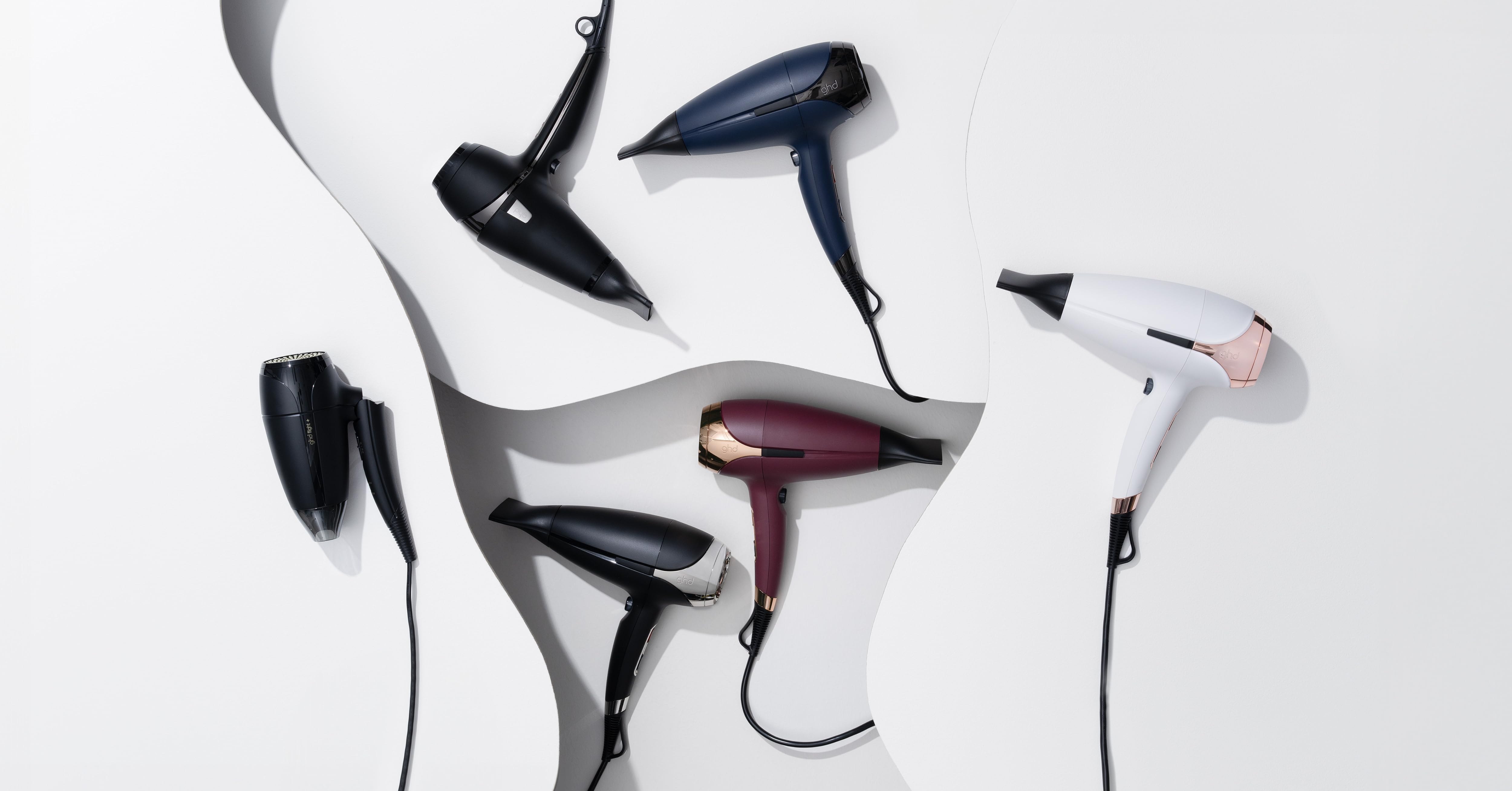 Surtido de secadores de pelo en varios colores, incluidos negro, azul marino, burdeos y blanco, dispuestos artísticamente sobre un fondo blanco con