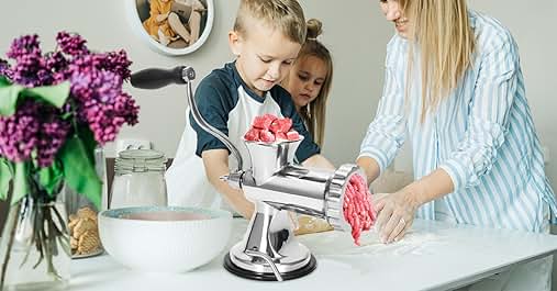 Metal meat grinder in use on kitchen counter. Two children and an adult operating it to process red meat. Bowls and lilacs visible.