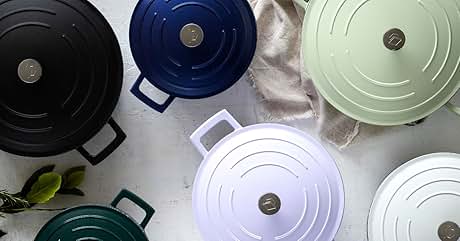 Assortment of round cooking pots with lids in various colors including black, blue, green, and white, arranged on a light surface.
