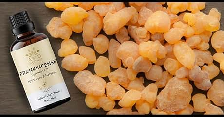 Brown glass bottle of frankincense essential oil next to pile of amber-colored frankincense resin pieces. Bottle label visible with product details.