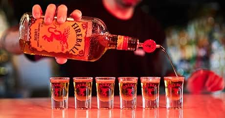 Se vierte licor de color naranja de una botella en seis vasos de chupito en la barra de un bar, lo que demuestra la técnica