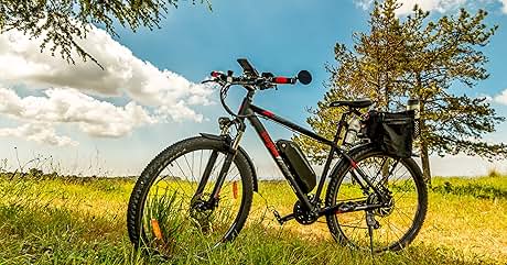 Bicicleta negra estacionada en un campo soleado con árboles de fondo. El cielo despejado y la hierba verde crean una escena exterior serena