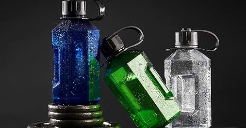 Three reusable water bottles in blue, green, and clear colors with black caps, arranged on a blue surface against dark background.