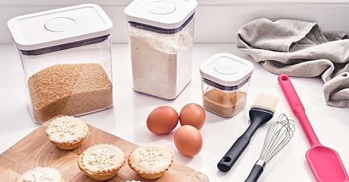 Set of clear plastic food storage containers with purple lids. Includes eggs, bread, measuring spoon, and kitchen towel.