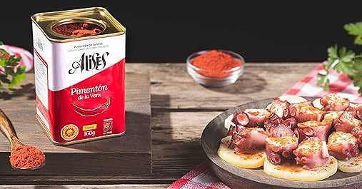 Tin of paprika next to plate of appetizers. Red spice in small bowl. Checkered cloth visible. Food styling scene on wooden surface.