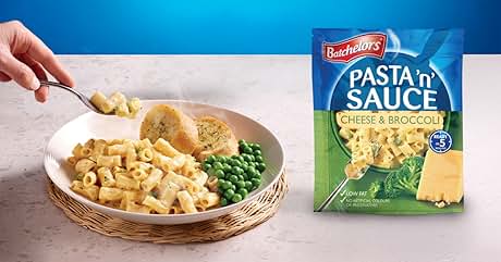 Batchelors Pasta n' Sauce cheese & broccoli flavor packet next to prepared dish with pasta, peas, and garlic bread on wicker plate. Hand adds grated cheese.