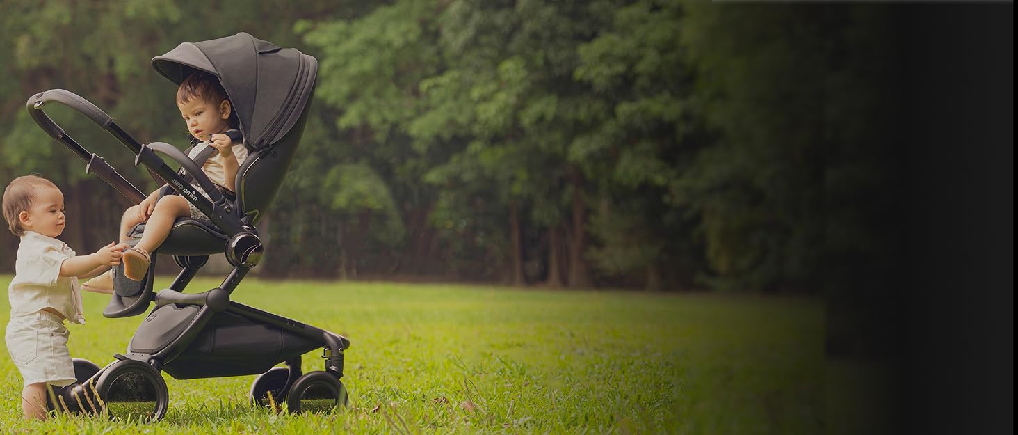 Two toddlers share a tender moment outdoors with a sleek, modern stroller in a natural setting.