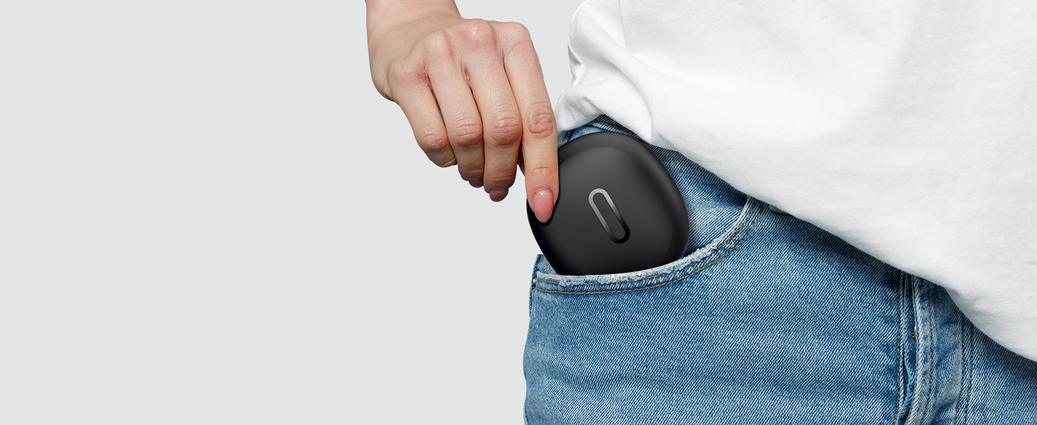 A black, oval-shaped electronic device being placed into the pocket of blue denim jeans. The device has a small curved indentation visible on its surface.