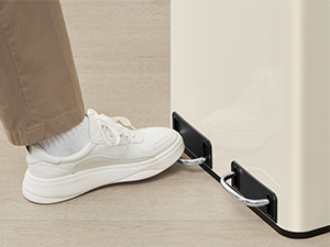 Közeli felvétel egy fehér tornacipőben lévő személy lábáról, amint egy alacsony profilú, falra szerelt eszközzel nyitja vagy zárja az ajtót.
