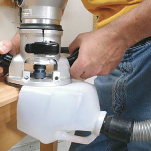 A milk jug is attached to a power tool and a shop vacuum hose as hands work the machine