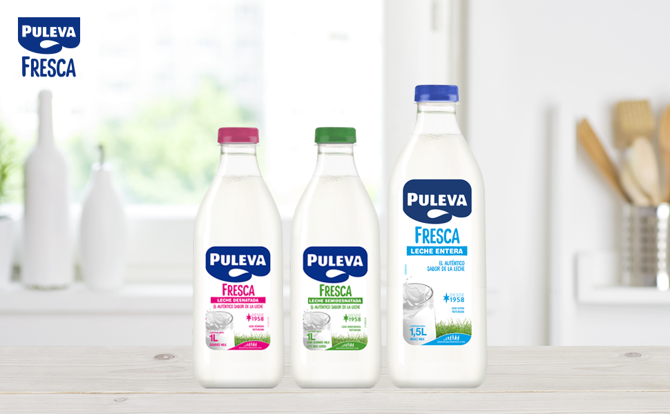 Tres botellas de plástico blancas de productos de la marca Prima dispuestas sobre la encimera de la cocina con fondo blanco y utensilios de madera. Las botellas tienen tapas rojas, verdes y azules.