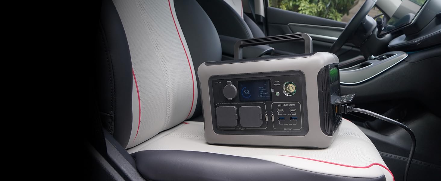 Black electronic device with control panel interface sitting on a car seat. Device has multiple buttons and ports visible on its surface.