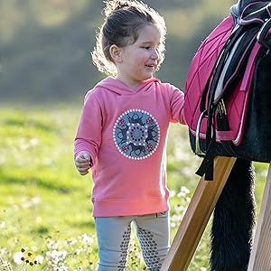 Rosa Kinder-Sweatshirt und Reitausrüstung werden draußen in einer sonnigen Feldumgebung ausgestellt.
