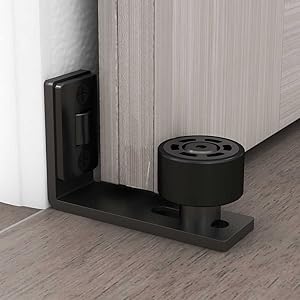 Black floor-mounted door stopper with adjustable roller wheel, installed on hardwood flooring next to a white door and wall.