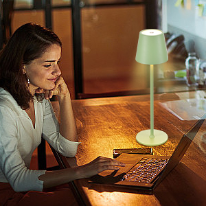 Persoon die op een laptop werkt aan een houten bureau met een kleine groene lamp die zorgt voor zachte verlichting in een slecht verlichte kamer