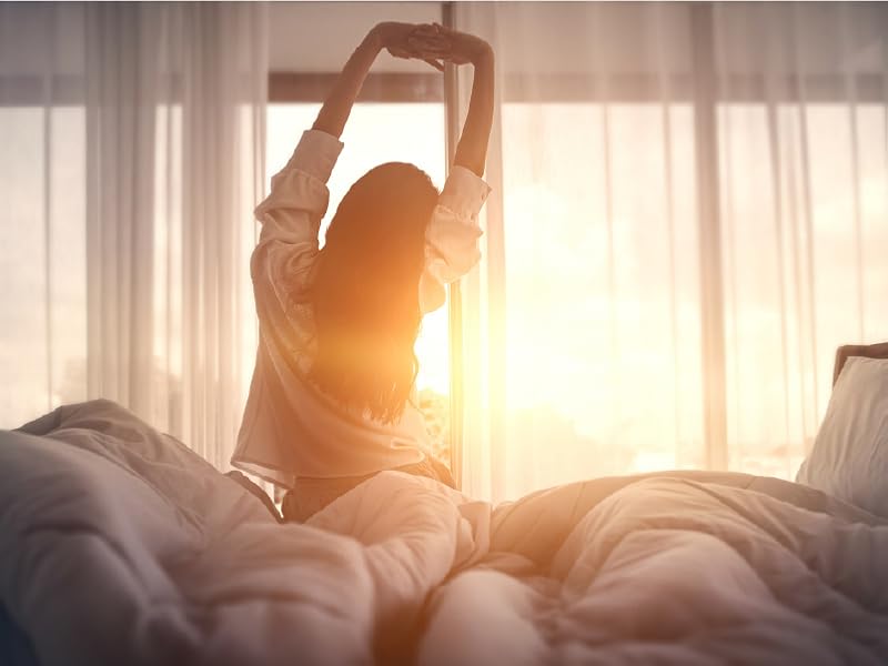 Woman stretching in bed while the sun rises through the window