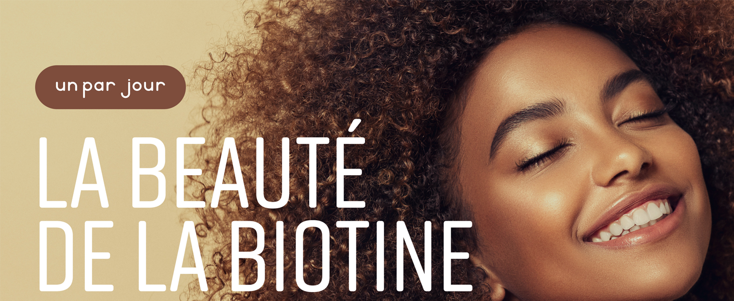Publicité de produit de beauté montrant des cheveux bouclés texturés sur fond beige. Le texte indique « LA BEAUTÉ DE LA BIOTINE » en lettres majuscules blanches