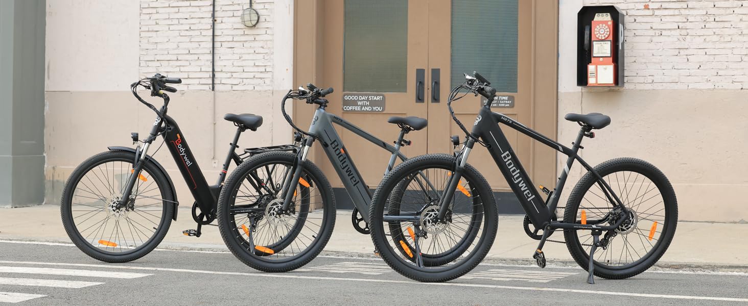Vier schwarze Elektrofahrräder, die in einer Reihe an einer weißen Backsteinmauer mit Glastüren geparkt sind und die urbane Straßenkulisse zeigen.