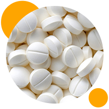 Vue rapprochée de comprimés ronds blancs ou de pilules avec des lignes de score, disposés selon une composition circulaire sur un fond blanc avec des accents circulaires orange