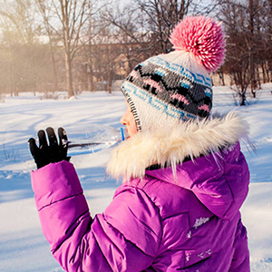 A child in black knit gloves strolls leisurely, sipping water, bathed in the setting sun.