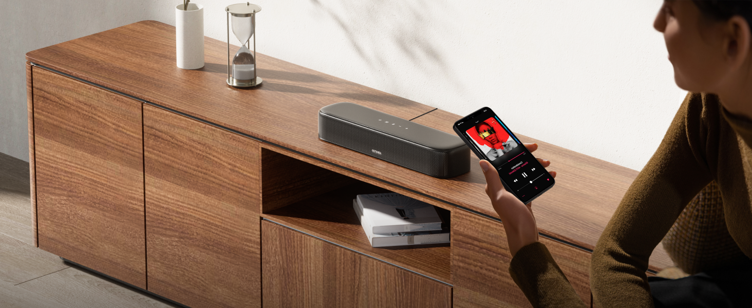 Wooden media console with person holding smartphone, demonstrating wireless charging or device interaction with the furniture.