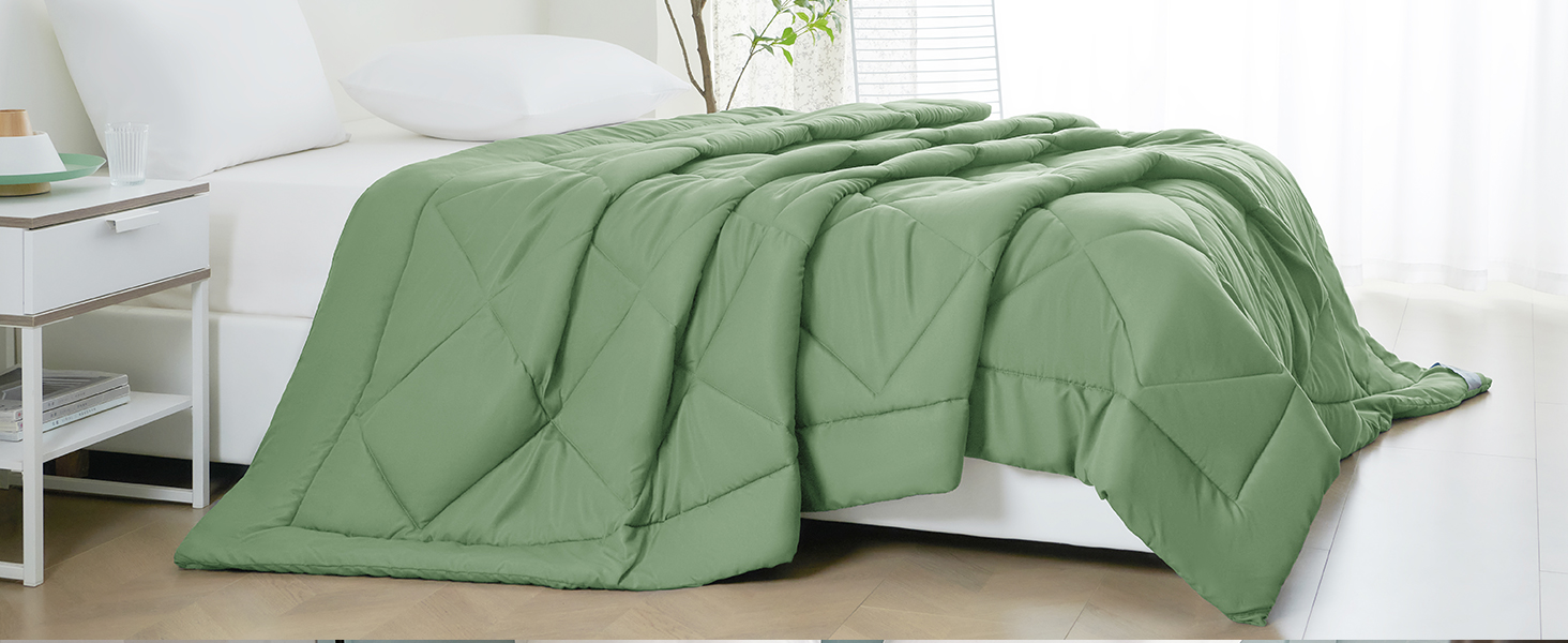 Sage green quilted comforter or duvet cover draped over a bed. The bedding features a diamond-shaped stitching pattern and appears soft and fluffy.