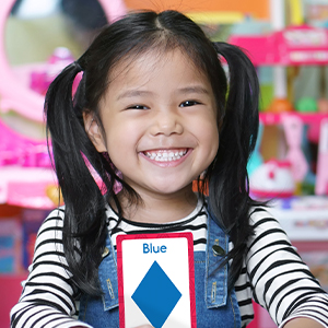 A young girl smiling holding a blue diamond flash card from the Early Learning Set