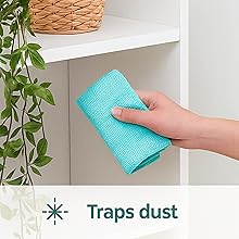 Microfiber cloth dusting shelves with decorative baskets.