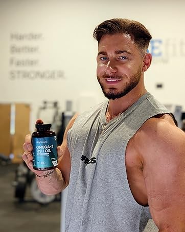 Athletic individual in a grey sleeveless shirt holding up a blue supplement container in what appears to be a gym setting.