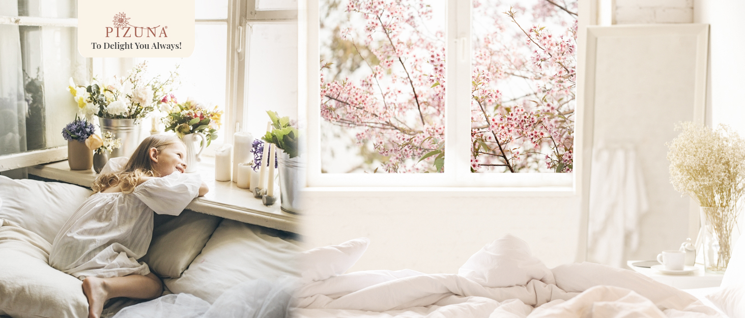 Bright, airy bedroom with person relaxing on white bedding. Large windows show cherry blossoms outside. Vases with flowers on windowsill.
