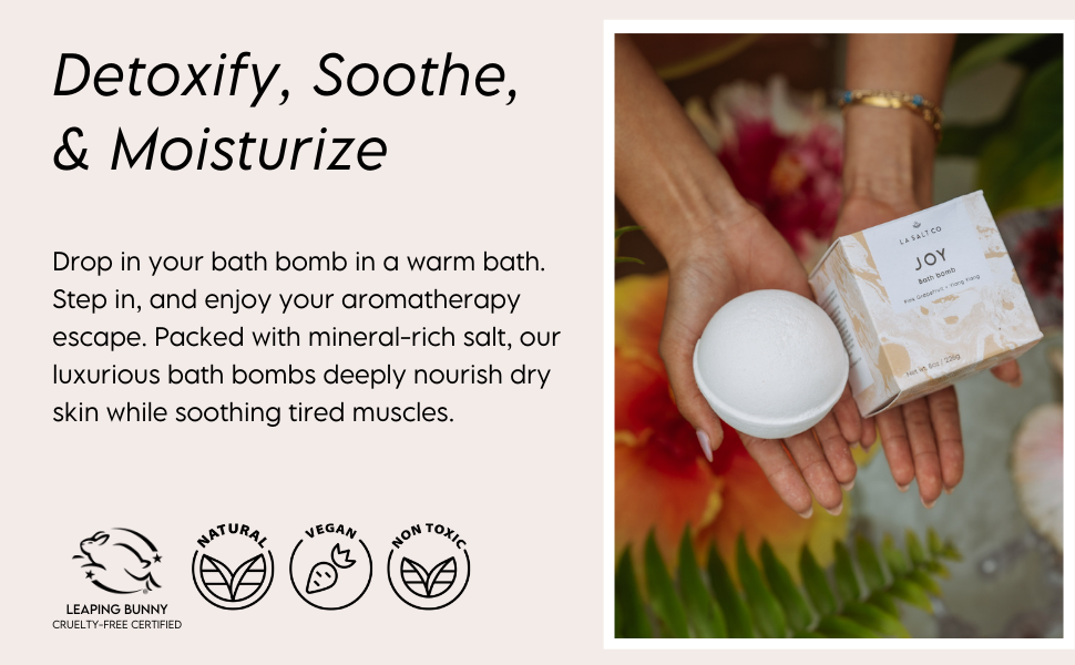 A female holding an LA SALT CO aromatherapy joy bath bomb over a tropical bath 
