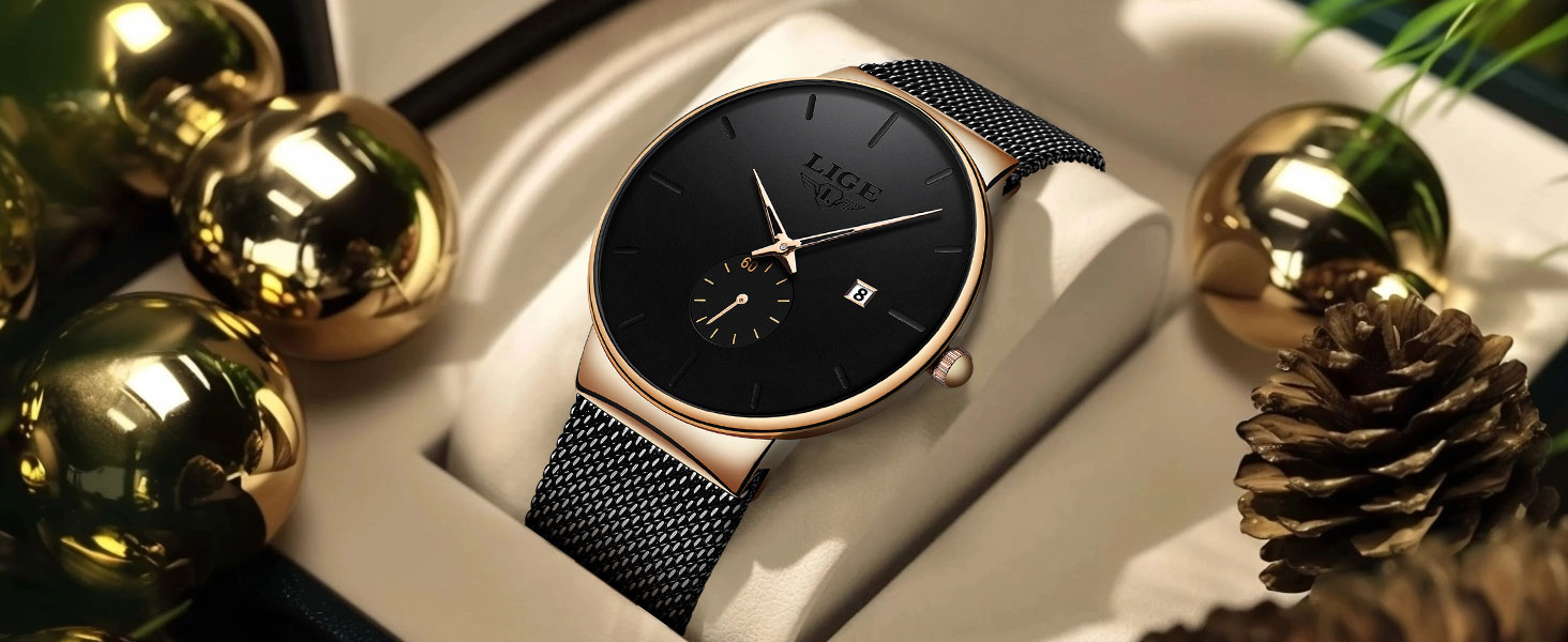 Minimalist wristwatch with black mesh strap, black dial, gold-tone case, and date display. Surrounded by gold ornaments and pinecone, suggesting luxury styling.