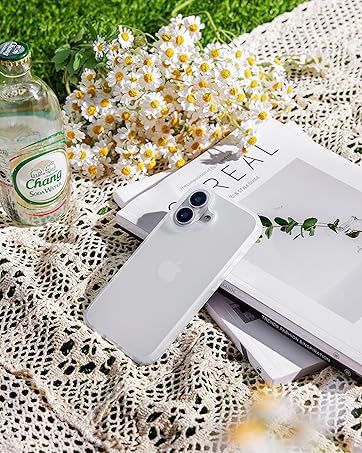 Silver smartphone on white lace surface with daisy flowers and glass bottle. Lifestyle product shot in outdoor setting with grass background.