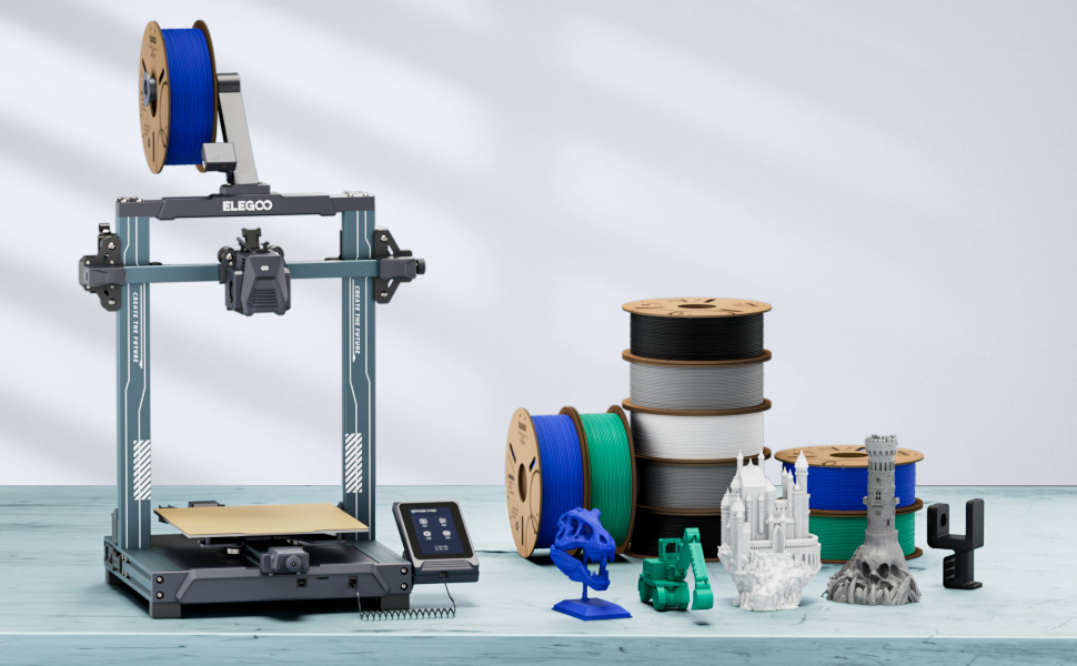 Configuração de impressora 3D com moldura azul, painel de controlo e vários carretéis de filamentos em várias cores. Objetos impressos e acessórios visíveis na mesa.