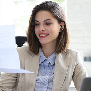 a woman working at a desk with a laptop and a document in her hand.