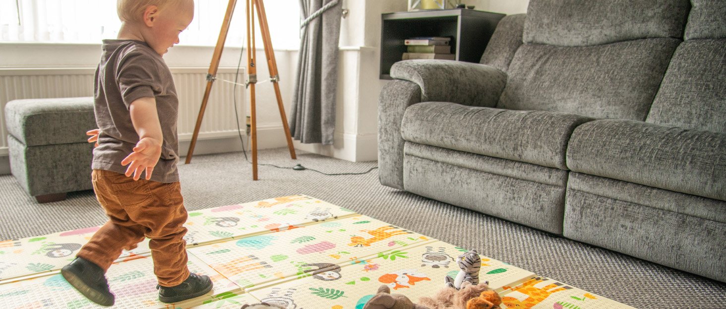 a younf blonde boy plays on a safari print nursery mat with plushie toys
