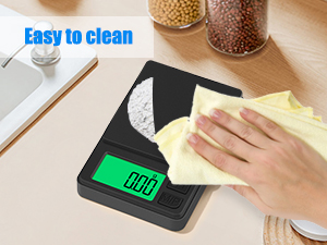 Digital kitchen scale with green LCD display being wiped clean with yellow cloth, demonstrating easy-clean surface feature.