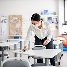 Masked teacher cleaning a students desk