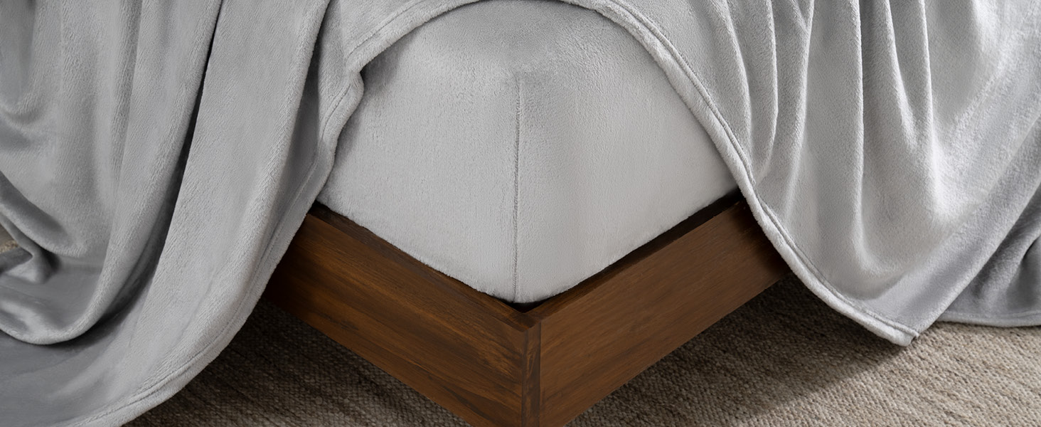 corner of a bed with a fitted sheet on and a flat sheet draped over the bed.